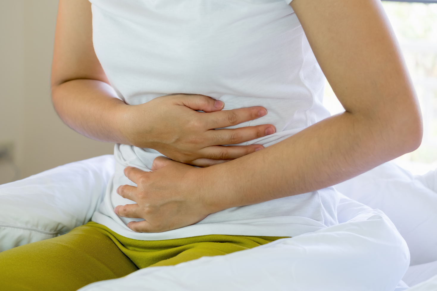 Asian Young Woman Suffering from Abdominal Pain While Sitting on