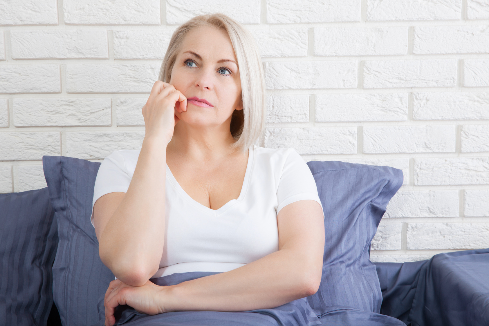 Sad woman sitting on the bed at the morning. Depressed menopause.